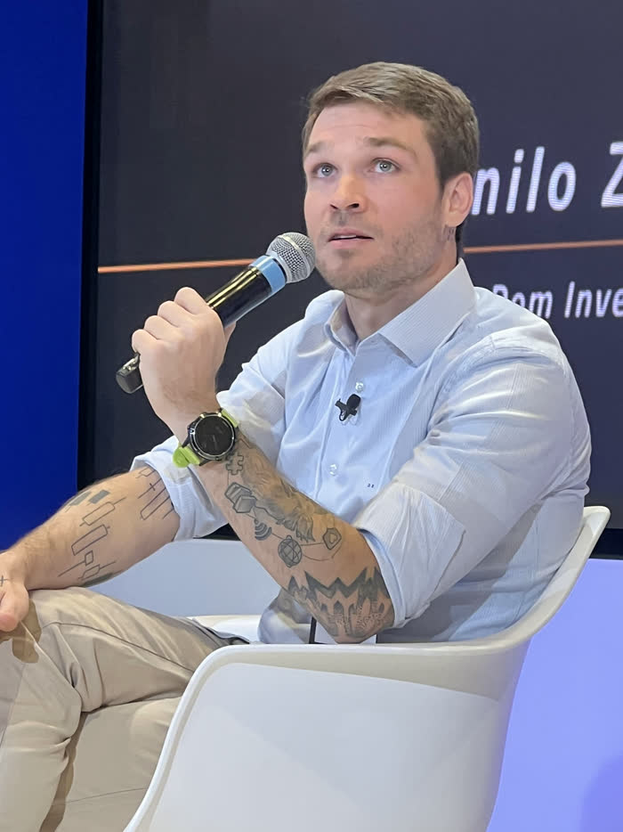 Danilo Zanini palestrando no palco, de microfone na mão, com o nome dele no telão